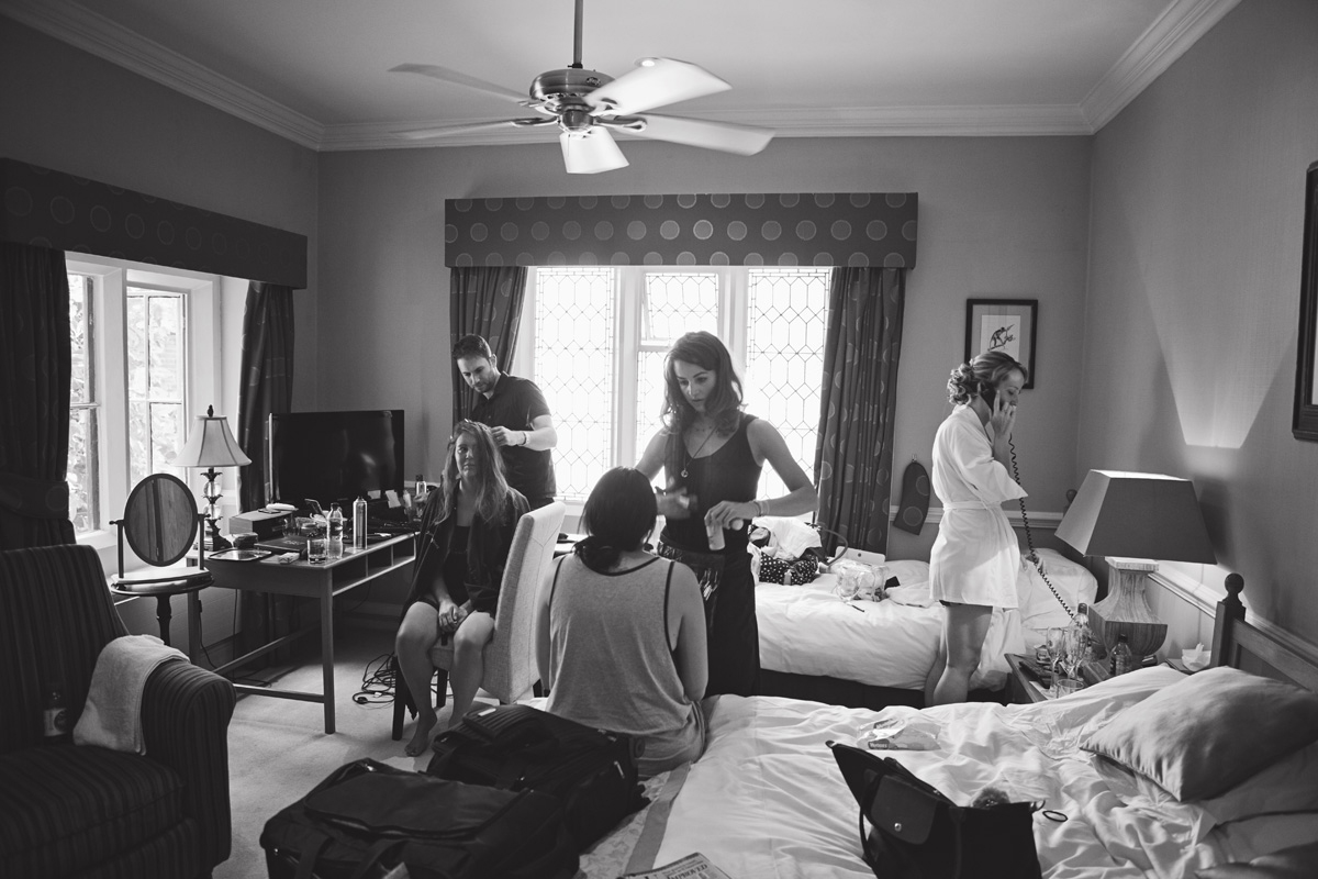 A black & white image of a bride and her bridesmaids getting dresses and made up in a hotel room