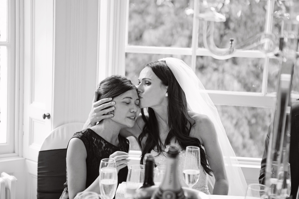 A bride kisses her bridesmaid on her forehead at her wedding breakfast